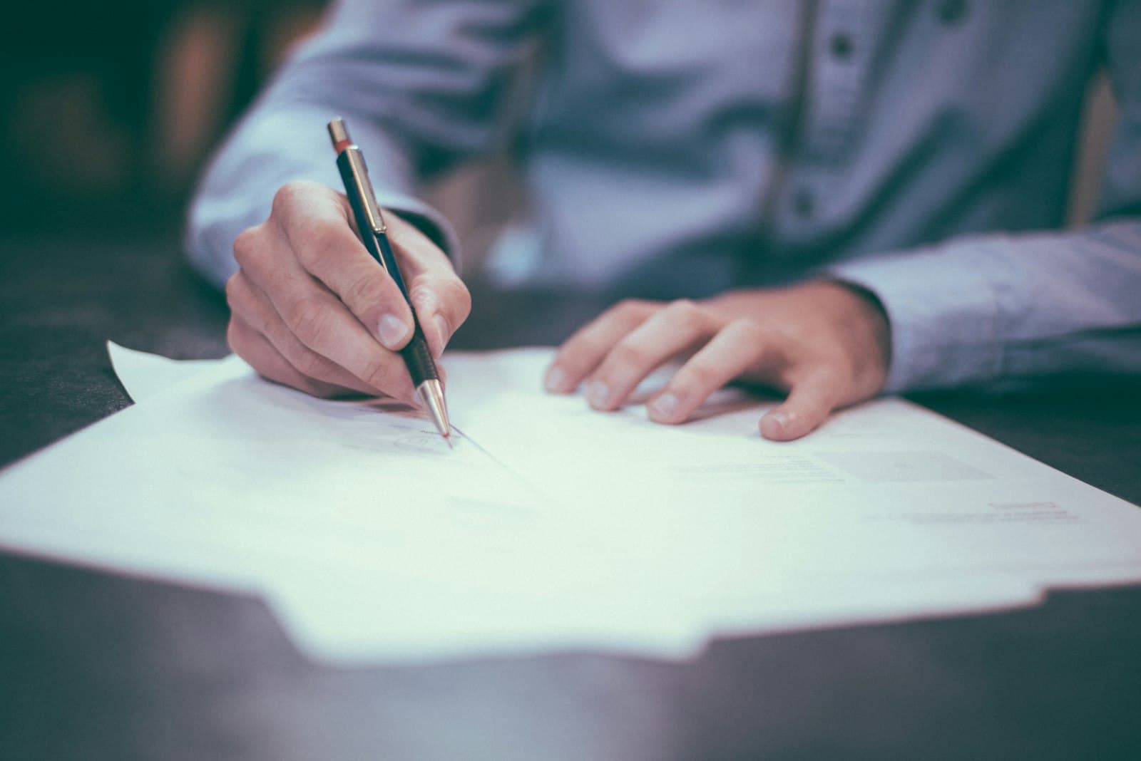 A person signing paperwork at a desk with a pen