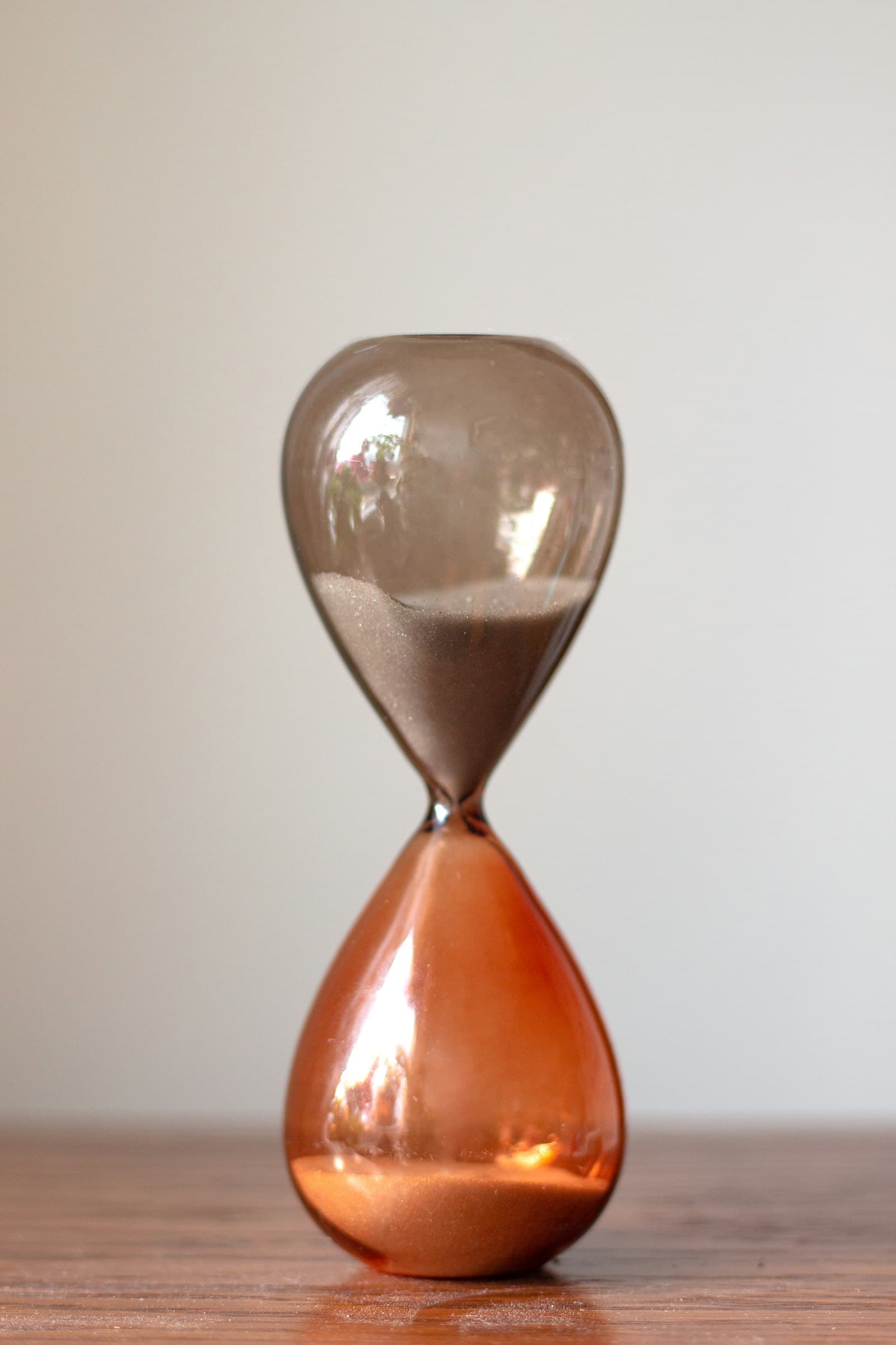 An hourglass with sand running down, standing on a wooden table